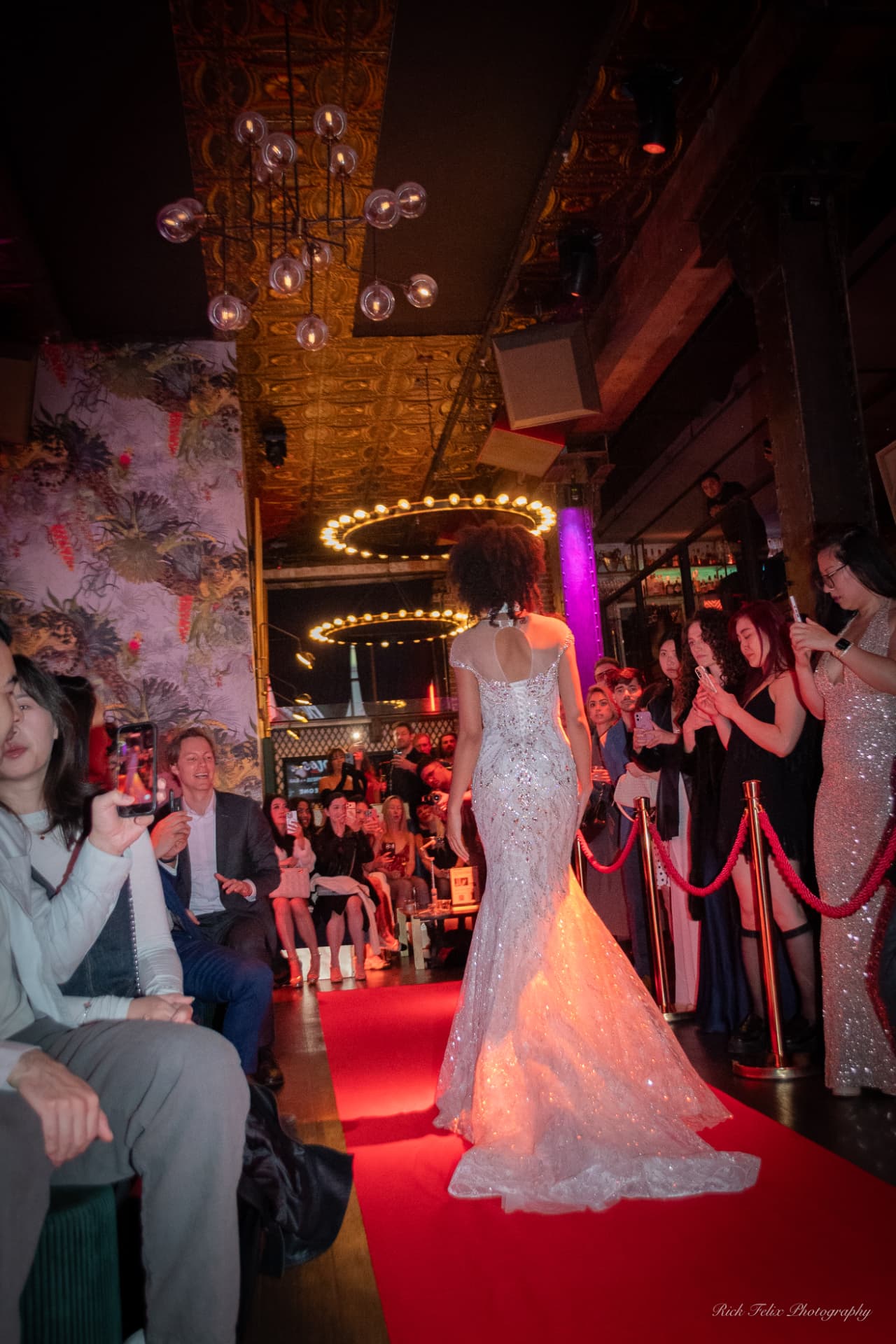 Model in a crystal-embellished gown walking the red runway as guests film