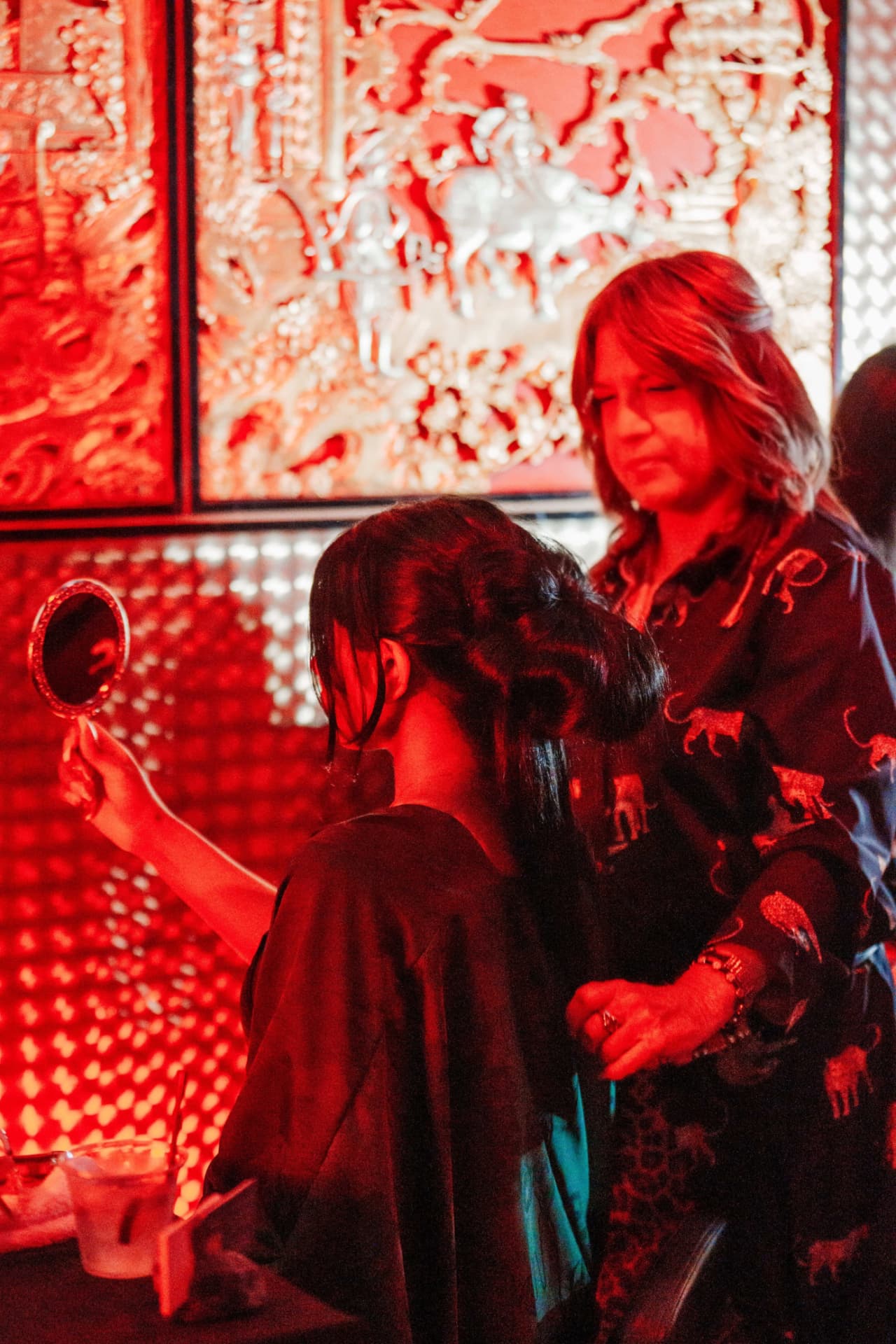 Guest holding a hand mirror while a stylist adjusts her look in red light